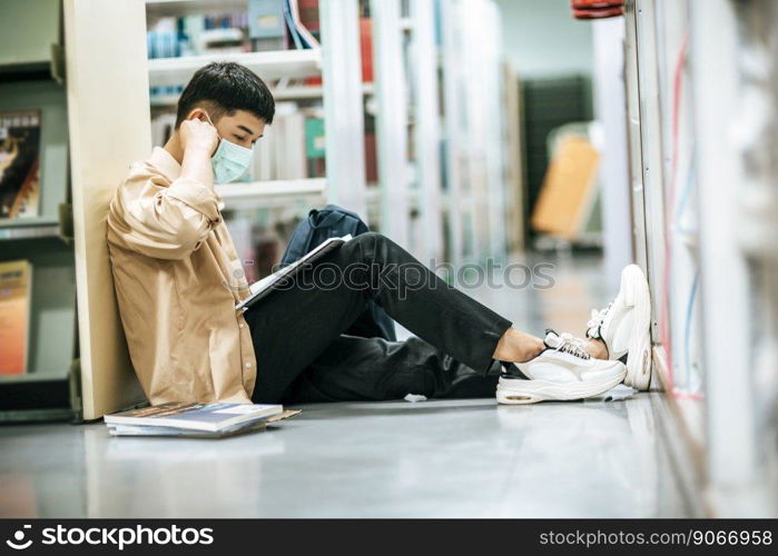 A man wearing masks is sitting reading a book in the library.