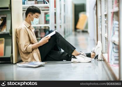 A man wearing masks is sitting reading a book in the library.