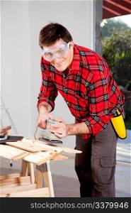 A man wearing saftey goggles using an electric hand sander