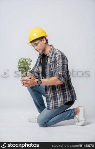 A man wears orange gloves and sit to hold a plant pot in the house.