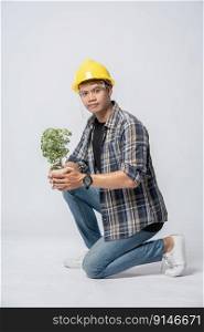 A man wears orange gloves and sit to hold a plant pot in the house.