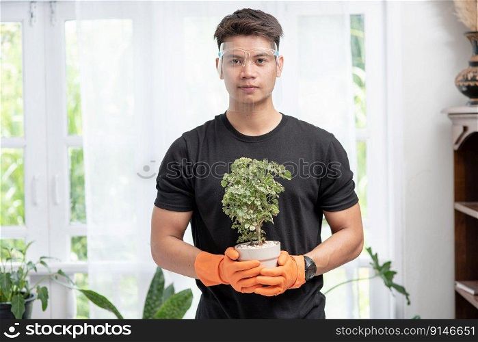 A man wears orange gloves and stands to hold a plant pot in the house.
