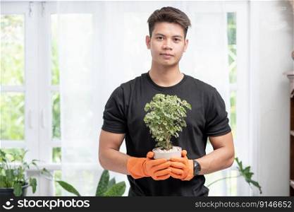 A man wears orange gloves and stands to hold a plant pot in the house.
