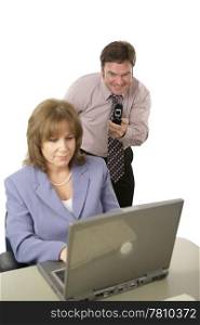 A man with a camera phone taking pictures of a coworker&rsquo;s computer screen behind her back. Isolated on white with focus on man.