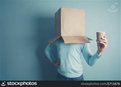 A man with a cardboard box on his head is holding a paper cup