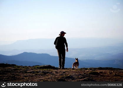 A man with a dog on a cliff above a mountain valley.. man with a dog on a cliff above a mountain valley.