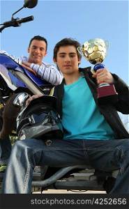 A man with a motorcycle and a trophy.
