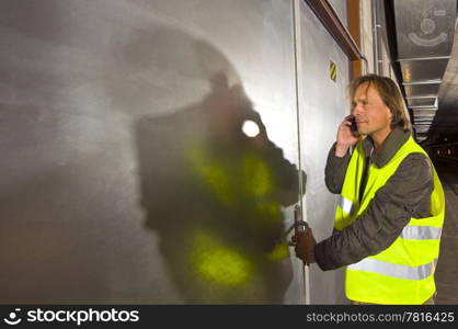 A man with a phone in his hand wearing a yellow reflective safety vestopening a steel door inside a tunnel