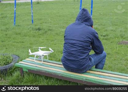 A man with a remote control quadroopter in his hands is sitting on a bench. White quadroopter prepare for flight. A man with a remote control quadroopter in his hands is sitting on a bench. White quadroopter prepare for flight.