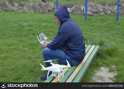 A man with a remote control quadroopter in his hands is sitting on a bench. White quadroopter prepare for flight. A man with a remote control quadroopter in his hands is sitting on a bench. White quadroopter prepare for flight.