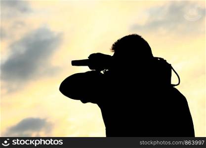 A man with TV camera on his shoulder silhoetted against sunset