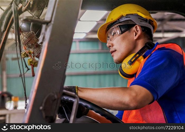 A man with yellow safety helmet and goggles driving a forklift or reach truck at the logistics warehouse store.