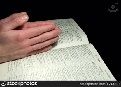 A mans hands clasped in prayer over a Bible