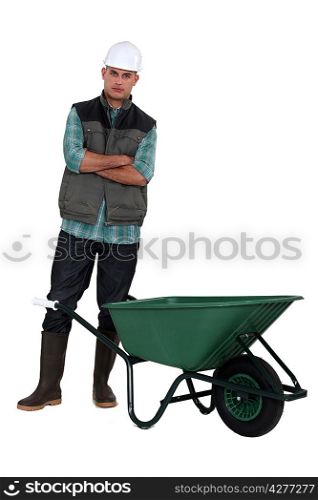 A manual worker standing by a wheelbarrow.