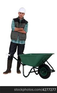 A manual worker standing by a wheelbarrow.