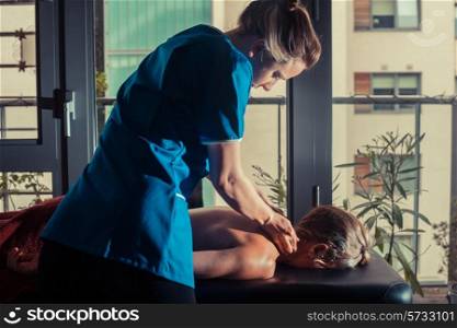A massage therapist is treating a female client on a table by the window