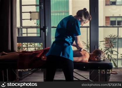 A massage therapist is treating a female client on a table by the window