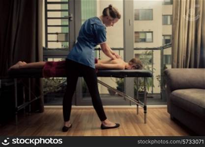 A massage therapist is treating a female client on a table in an apartment