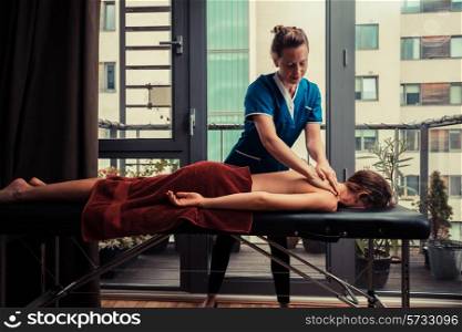 A massage therapist is treating a female client on a table in an apartment