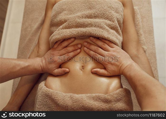 A masseur pampering the stomach to young woman in towel, professional massage. Massaging and relaxation, body and skin care. Attractive lady in spa salon. A masseur pampering stomach to young woman