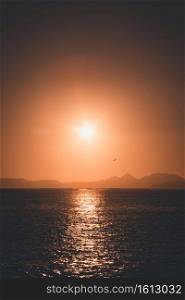 A massive sunset over the islands reflecting over the ocean with the sun and the tides on the beach over the sand during spring, on colorful tones with copy space