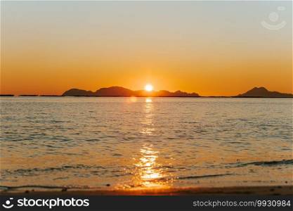 A massive sunset over the islands reflecting over the ocean with the sun and the tides on the beach over the sand during spring, on colorful tones with copy space