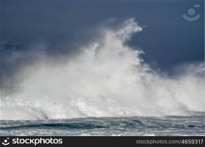 A massive wave crashes against a reef in the ocean sending water spraying high up in the air.