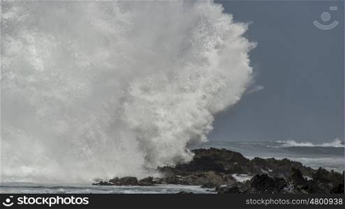 A massive wave crashes against the rocks at the shoreline at Storms River Mouth and creates a big splash.