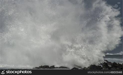 A massive wave explodes and disintergrates as it brakes on the shoreline