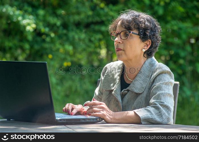 a mature brunette using laptop in the garden