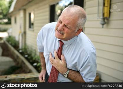 A mature businessman doubled over clutching his chest. He appears to be having a heart attack.