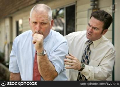 A mature businessman with a severe cough. His worried colleague is patting him on the back. Focus on coughing man.