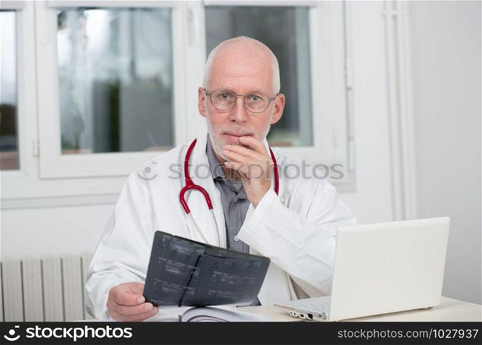 a mature doctor examining x-ray, at his office