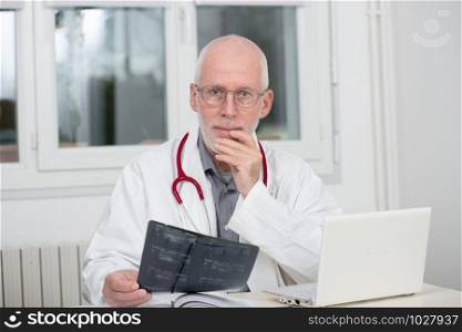 a mature doctor examining x-ray, at his office