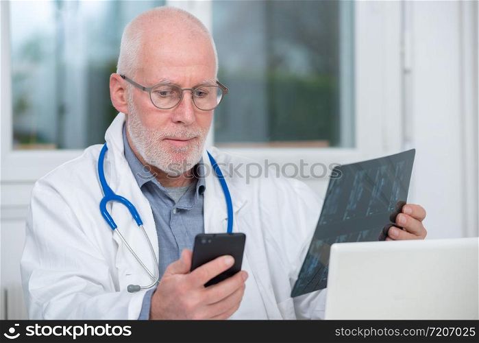 a mature doctor looking at x-ray picture and using telephone