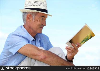 A mature man reading a book outside.