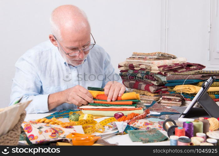 a mature man tailor choosing some fabric