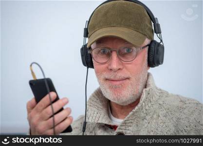 a mature man with cap in headphones listening to music at home