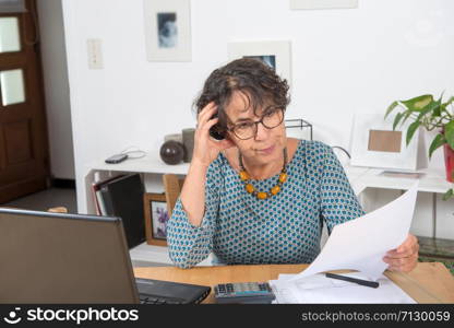 a mature woman paying bills with laptop at home