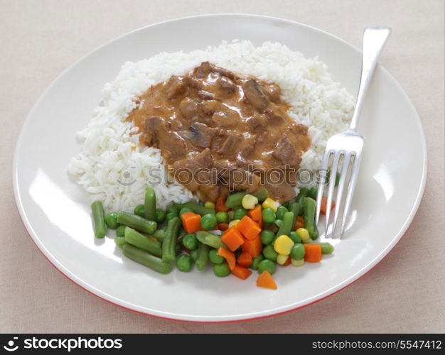 A meal of beef stroganoff and rice, served with boiled mixed vegetables