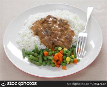 A meal of beef stroganoff and rice, served with boiled mixed vegetables