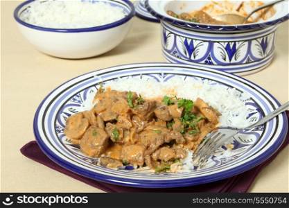 A meal of beef stroganoff with white rice and a fork on a table.