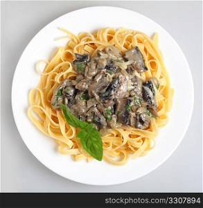 A meal of fettuccini with mushrooms, onion and garlic in a cream and parsley sauce, served with a sprig of basil.