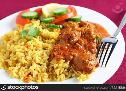 A meal of Kashmiri lamb curry with rice and salad on a maroon tablecloth.