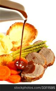 A meal of roast beef with carrots, Yorkshire puddings, potatoes and asparagus, with gravy being poured on