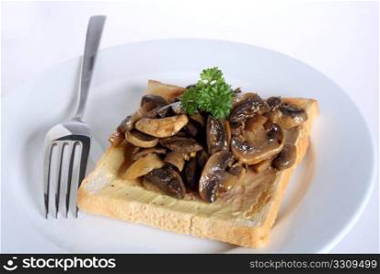 A meal of sauteed mushrooms on toast on a white plate with a fork