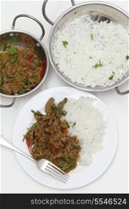 A meal of spiced lamb curry with coriander leaves and slivers of red and green chillies, served with plain boiled rice, viewed from above.