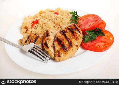 A meal of spicy grilled cajun chicken breasts with vegetable rice and fresh tomato