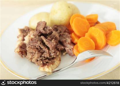 A meal of steak and kidney pudding served with boiled new potatoes and sliced carrot