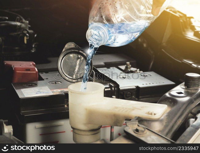 A mechanic hand was putting clean water into the car engine windshield wiper water reserve tank